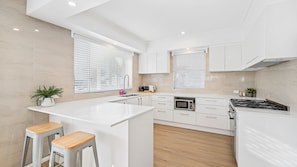 Una cocina moderna con armarios blancos, una isla central, taburetes de bar y un microondas.