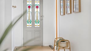 Una puerta blanca con vidrieras, piso de madera, una alfombra pequeña y una silla de mimbre.