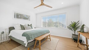 Quarto com cama, mesa de cabeceira, abajur e ventilador de teto.