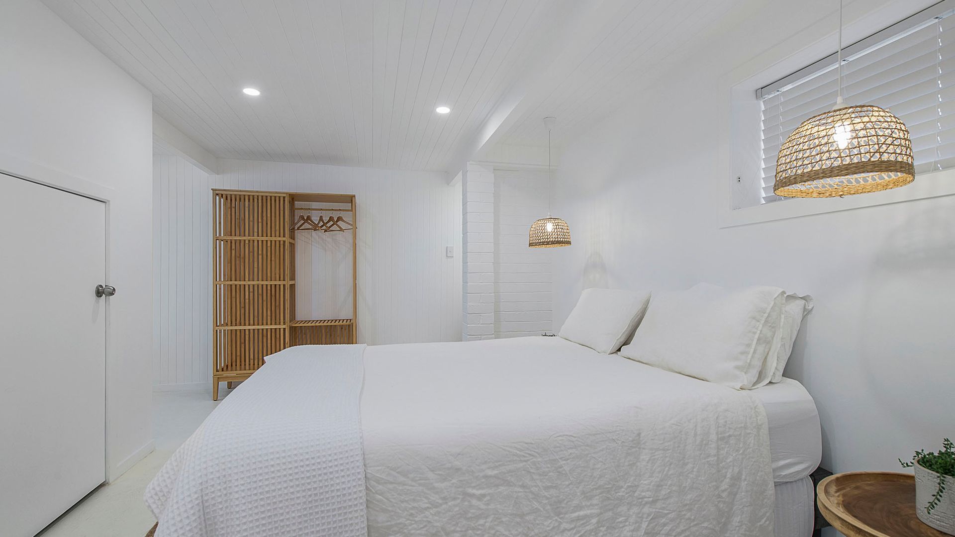 A bedroom with a large bed, a wardrobe, a hanging wardrobe, and a window with blinds.