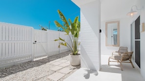 A white building with a paved patio, a potted plant, and wicker furniture.