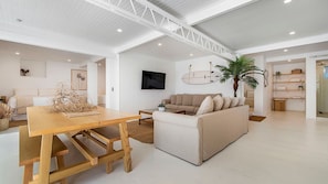 A spacious living area with a wooden dining table, a beige sofa, and a television mounted on the wall.