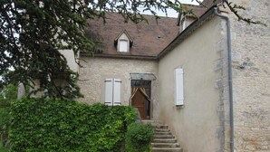 A stone building with a small garden, a white table with chairs, and a staircase leading to a door.