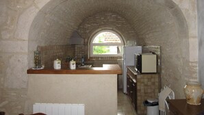 A kitchen with an arched stone ceiling, a window, and basic amenities including a refrigerator, sink, and cabinets.