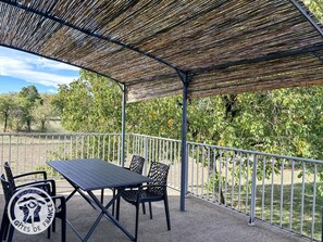 An outdoor patio with a table and chairs, a metal railing, and a thatched roof. - Gîtes de France® - Chalvet cottage (BASTIT (LE))