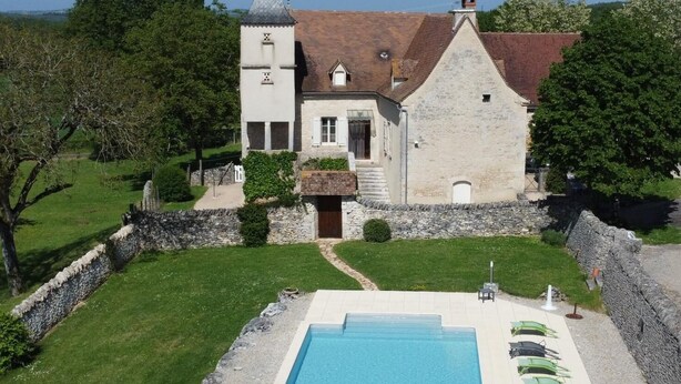 A stone building with a swimming pool, surrounded by a stone wall and greenery.