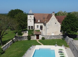 Edifício de pedra com piscina, cercado por um muro de pedra e vegetação.