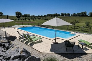 A rectangular swimming pool with a tiled deck, surrounded by green lounge chairs and umbrellas.