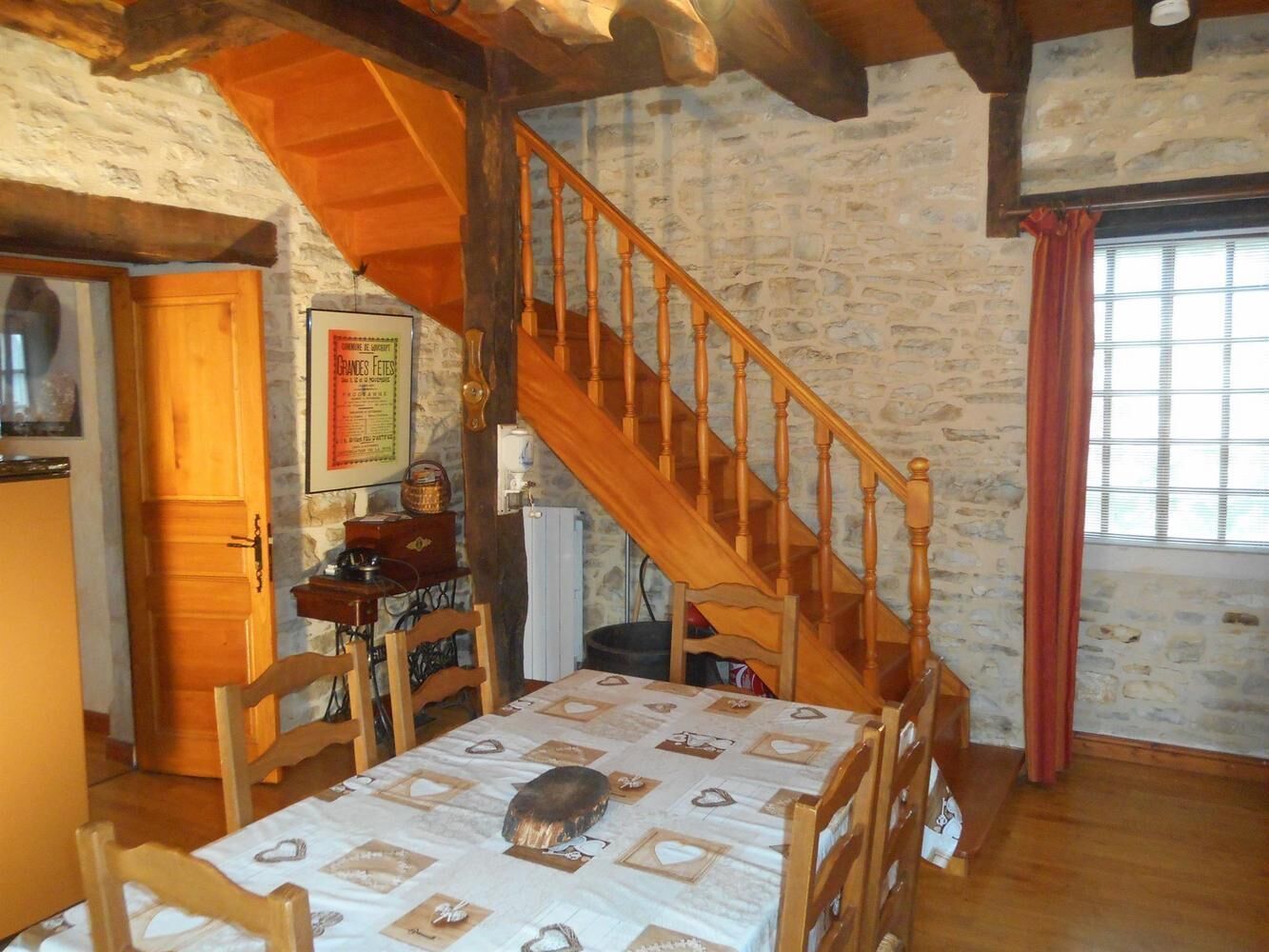 Una habitación rústica con una escalera de madera, una mesa de comedor con mantel estampado y una pared de piedra.