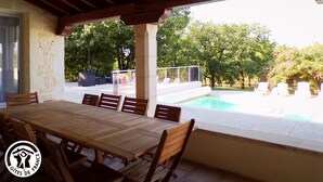 Ein überdachter Essbereich mit Pool im Hintergrund.