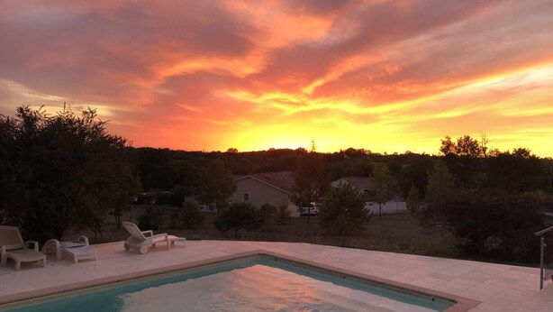 Ein Swimmingpool mit Liegestühlen, umgeben von Bäumen und Häusern, während der Sonnenuntergang stattfindet.