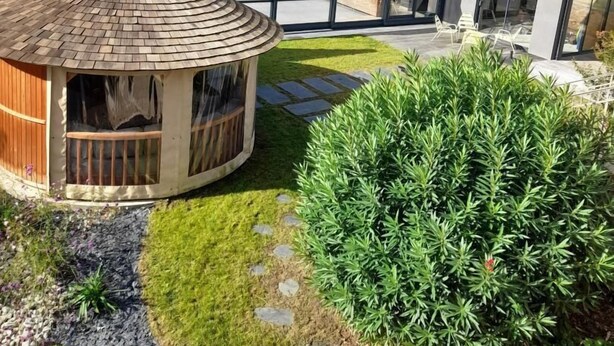 Una casa moderna con una estructura de madera circular, un porche cubierto y un jardín bien cuidado.