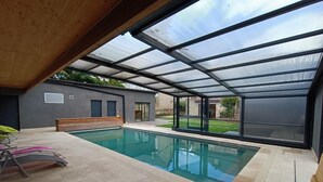 Una piscina interior moderna con techo de vidrio, suelo de baldosas y un banco.