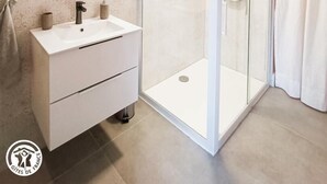 Ein modernes Badezimmer mit Duschkabine aus Glas, einem weißen Waschbecken und einem Waschtisch mit Schubladen.
