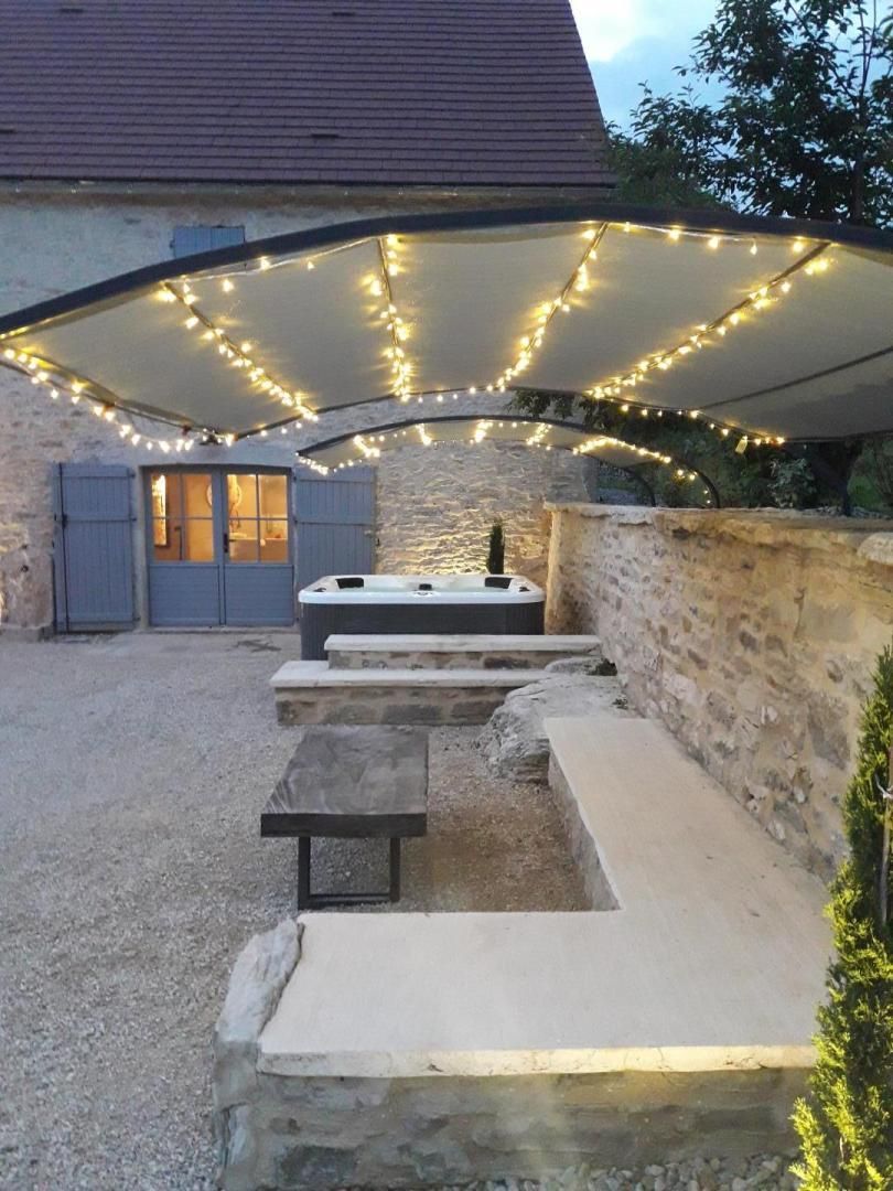 Un espace extérieur aménagé en terrasse, avec un banc en pierre, un jacuzzi et des guirlandes lumineuses.