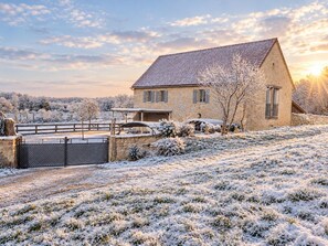 Una casa de piedra con techo inclinado, un camino de entrada con portón y un paisaje cubierto de nieve.