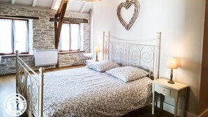 Ein Schlafzimmer mit Bett, Nachttischen, einer herzförmigen Dekoration und einem Fenster mit Vorhängen.