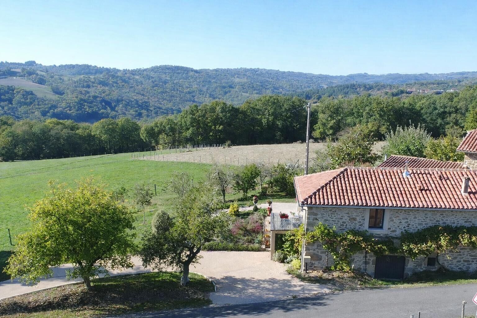 Paisaje rural con un edificio de piedra, un camino pavimentado y un campo cercado.