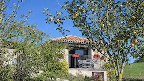 A house with a tiled roof, a balcony with chairs, and a garden with trees and shrubs. - Gîtes de France® - 46G12361 (VIAZAC)