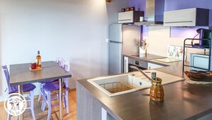 A modern kitchen with a dining area, featuring a wooden ceiling, a built-in oven, and a coffee machine. - Gîtes de France® - 46G12361 (VIAZAC)