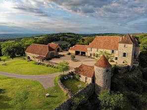 Ein historisches Steinhaus mit Innenhof, Turm und umgebender Bepflanzung.