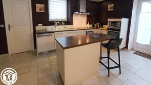 A modern kitchen with a central island, white cabinetry, a microwave, and a dishwasher. - Chez Yvette - Saint-sozy (SAINT-SOZY)