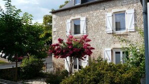 A stone building with white shutters, a balcony, and a flowering tree in the foreground. - Chez Yvette - Saint-sozy (SAINT-SOZY)