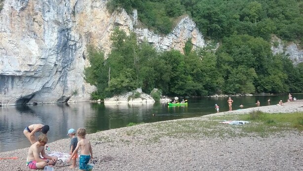 A rocky riverbank with people engaging in water activities and a green kayak. - Chez Yvette - Saint-sozy (SAINT-SOZY)