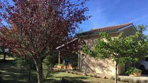 A house with a tiled roof, a covered patio, and a lawn with trees. - Gîtes de France® - 46G1905 (SAINT GERY-VERS)