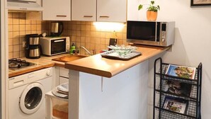 A compact kitchen with white cabinets, a wooden countertop, a washing machine, a microwave, a toaster, and a small sink. - Gîtes de France® - 46G1905 (SAINT GERY-VERS)