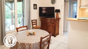 A dining area with a round table, chairs, a television, and a kitchen area with a counter and cabinets. - Gîtes de France® - 46G1905 (SAINT GERY-VERS)