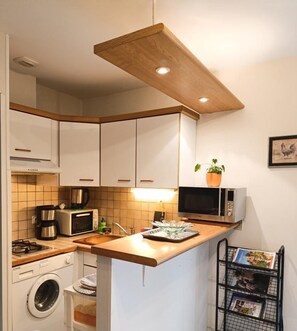 Une cuisine compacte avec des meubles blancs, un plan de travail en bois, un lave-linge, un four à micro-ondes, un grille-pain et un petit évier.