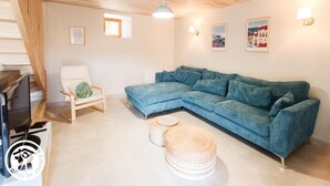 Ein gemütliches Wohnzimmer mit einer Eckcouch, einem kleinen runden Hocker und einem weißen Sessel.