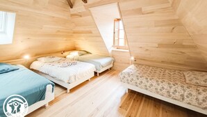 Ein gemütliches Schlafzimmer im Dachgeschoss mit Holzwänden und geneigten Decken, ausgestattet mit drei Betten und einem kleinen Fenster.