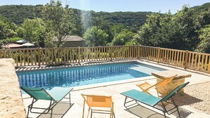 Ein rechteckiger Swimmingpool mit umlaufender Holzterrasse, ausgestattet mit Liegestühlen und einem Holzzaun.