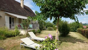 A house with a garden, a tree, and two sun loungers.