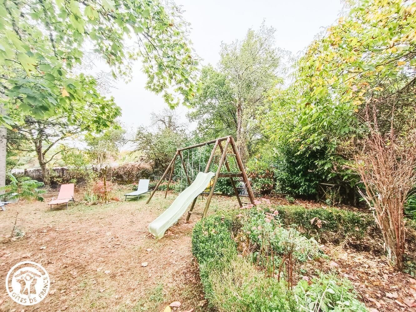 A playground with a slide and swings, surrounded by trees and shrubs.