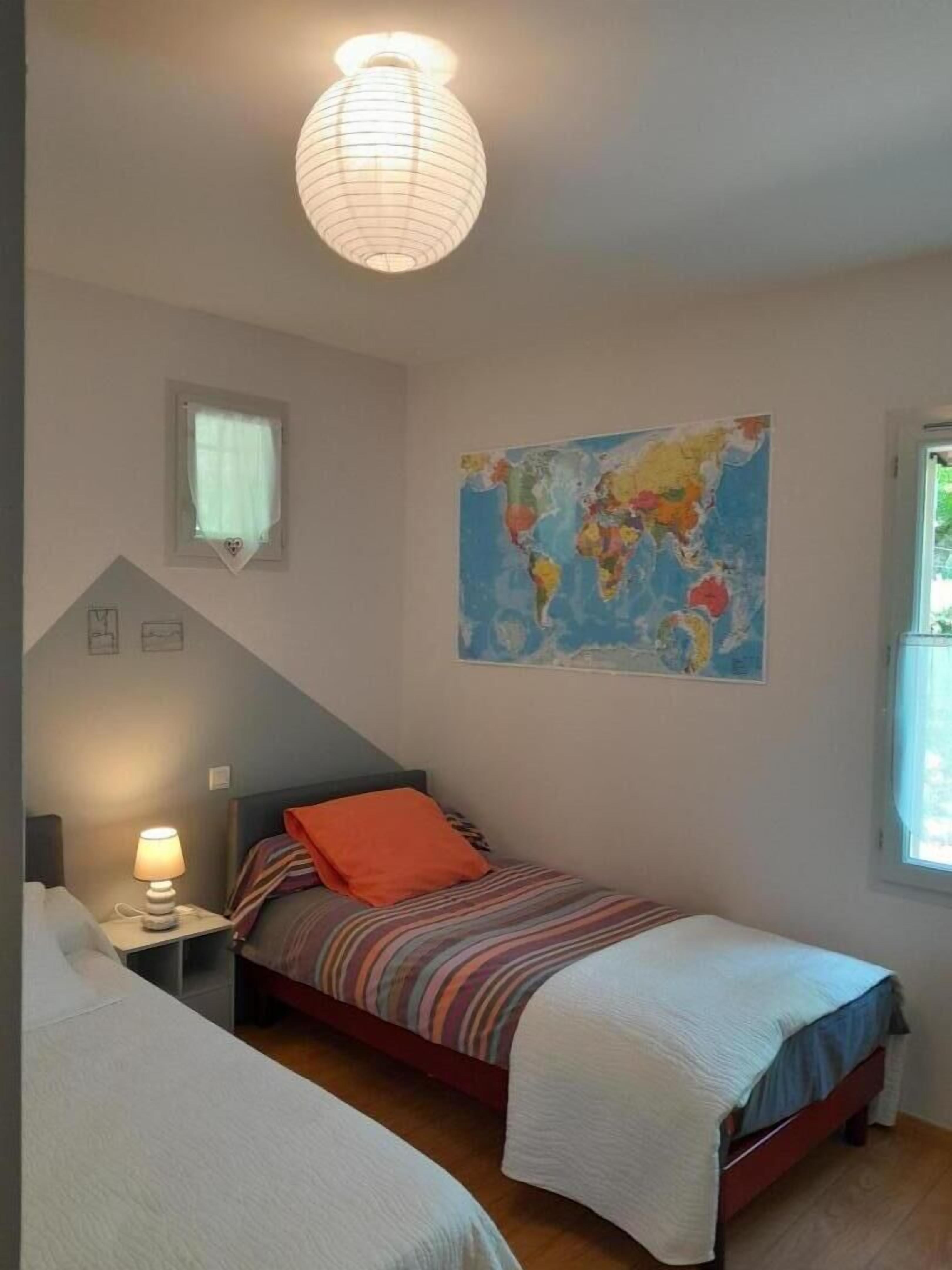 A bedroom with two beds, a world map on the wall, a lamp, and a window.