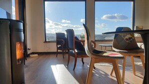 Ein Zimmer mit großem Fenster, Kaminofen und zwei Stühlen.