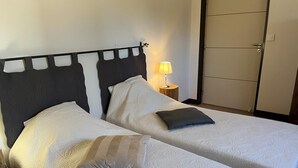 Ein Doppelbett mit dunklem Kopfteil, zwei Kissen, ein Nachttisch mit Lampe und ein Kleiderschrank im Hintergrund.