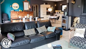 Een moderne woonkamer met een zwarte leren bank, een eethoek met een houten tafel en stoelen, en een keuken met een fornuis en kastjes.