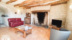 A cozy living room with a stone fireplace, a red leather sofa, a wooden coffee table, and a television on a wooden stand. - Gîtes de France® - Gîte de Costemagre (REILHAC)
