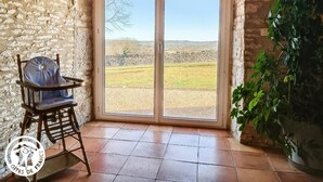 A room with a stone wall, a wooden chair, a large sliding glass door leading to an outdoor view, and a potted plant. - Gîtes de France® - Gîte de Costemagre (REILHAC)
