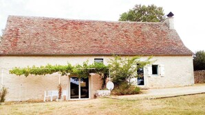 A rustic stone building with a tiled roof, a covered outdoor seating area, and a small garden. - Gîtes de France® - Gîte de Costemagre (REILHAC)