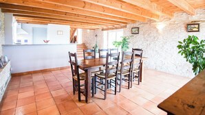 A dining area with a wooden table and chairs, stone walls, and a tiled floor. - Gîtes de France® - Gîte de Costemagre (REILHAC)