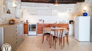 Een landelijke keuken met zichtbare houten balken, een centraal eiland met stoelen, een witte koelkast en een fornuis.