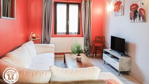 A cozy living room with a white sofa, a wooden coffee table, a TV stand, and a window with curtains.