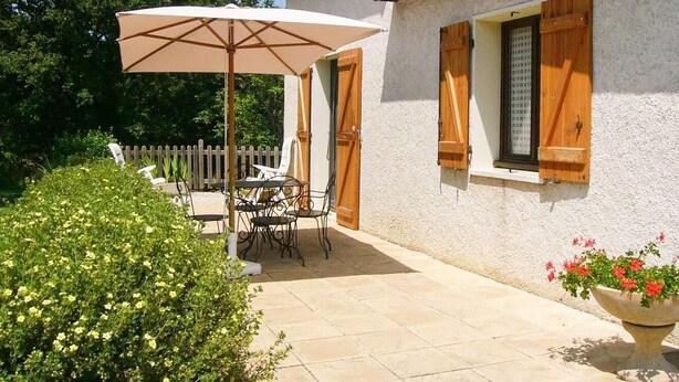 A patio with a table and chairs, a large umbrella, and a potted plant.
