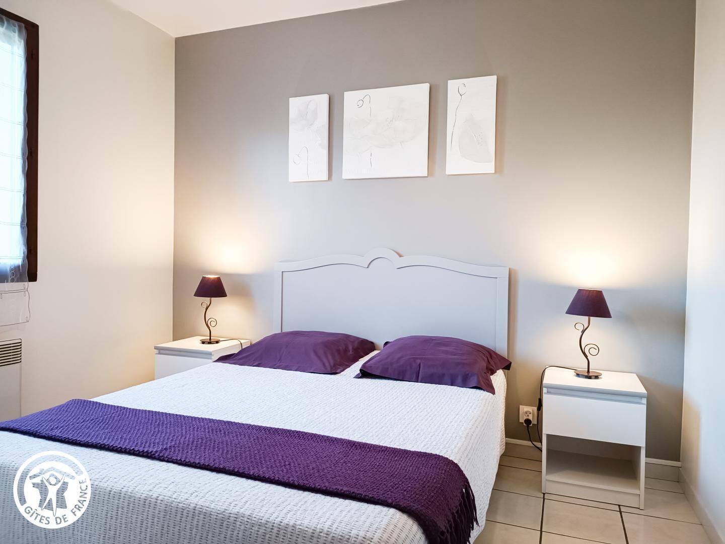 Een slaapkamer met een bed, twee nachtkastjes met lampen en drie kunstwerken aan de muur.