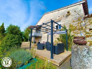 Un terrazzo in legno con posti a sedere all'aperto, un muro in pietra e una struttura in pergola metallica.